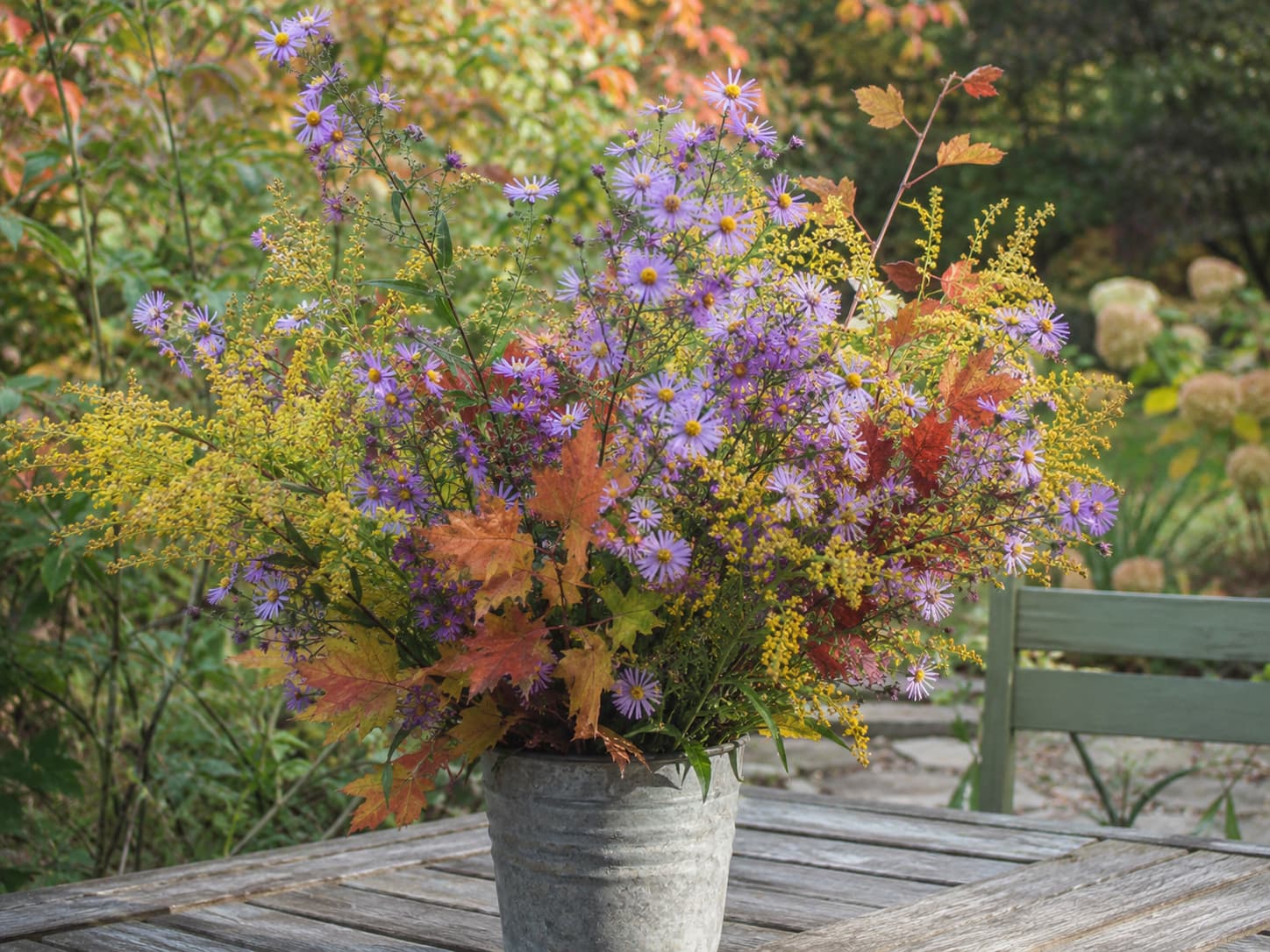 Fresh New England aster flowers arranged with goldenrod and autumn foliage in a natural fall centerpiece.